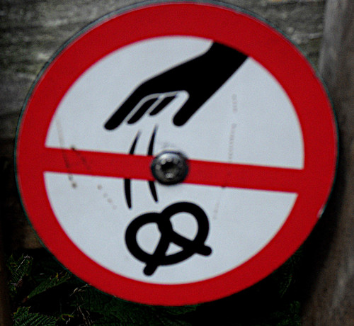 Verbotsschild. Eine Hand wirft eine Brezel weg, roter Rahmen und rot durchgestrichen.