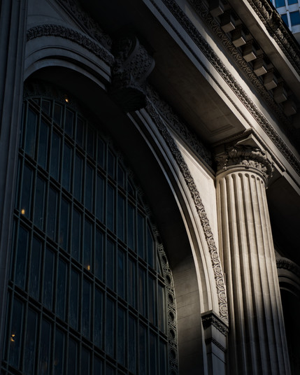 Sunlight hits the top of a fluted Doric column set next to an arched window in the main facade of the Grand Central Terminal train station, New York City, USA