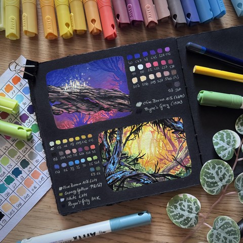 A photo of an open square sketchbook placed on a wooden desk and surrounded by acrylic markers, coloured pencils, a swatch card, and leaves for decoration. The sketchbook page features two little colourful sceneries with swatches next to them. The top one shows a thick branch with glowing white mushrooms on it, the background in blue/purple/red tones. The bottom one shows a dense forest with yellowish/orange light in the background and branches with tiny blue glowing fungus in the front.